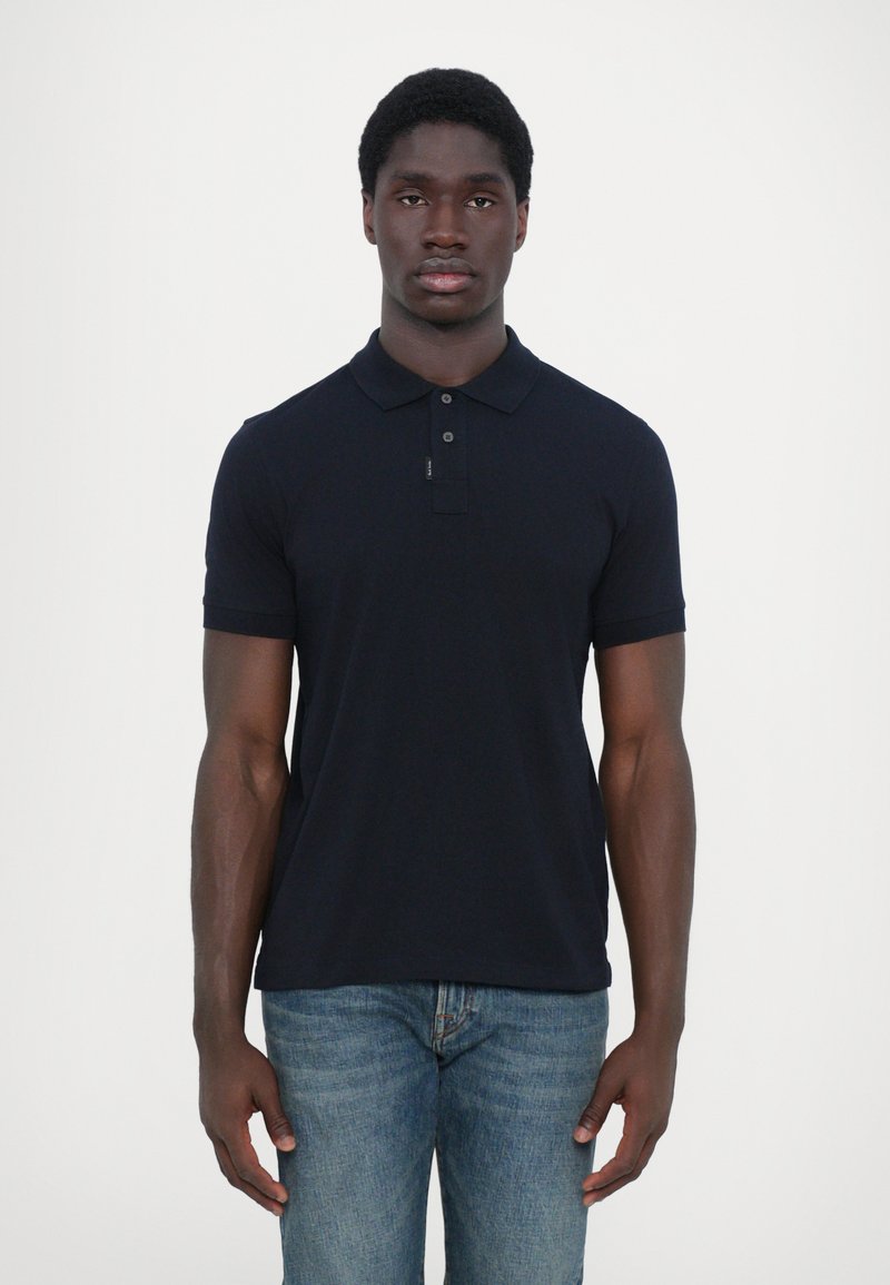 Navy polo shirt with a collared neck, three buttons, short sleeves, and a fitted design. Worn with light blue denim jeans.