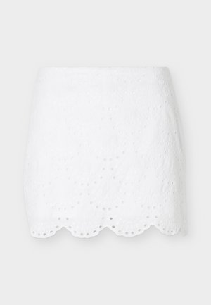 Λευκή μίνι φούστα με κέντημα με τρύπες, κυματιστό τελείωμα και λουλουδάτα μοτίβα με κοψίματα, παρουσιάζεται σε απλό ανοιχτό γκρι φόντο.