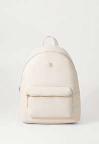 Sac à dos en cuir blanc avec une forme arrondie, une quincaillerie dorée et une poche avant zippée. Texture lisse et design minimaliste.