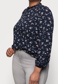 Marinblomstrig blus med samlad halsringning, långa ärmar med elastiska muddar och rosa blomster mönster på lätt tyg.