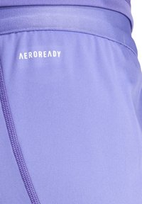 Paarse sportshorts gemaakt van soepel, rekbaar materiaal met een ritszak aan de zijkant en het 'AEROREADY'-logo in het wit.