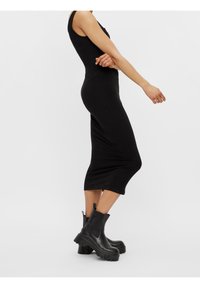 Svart ribbad midiklänning med en figurnära silhuett, med breda axelremmar och rundad hals, ihop med kraftiga svarta ankelskor.