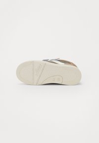 Semelle de sandale avec une surface en caoutchouc blanc texturé, dotée de brides marron, argent et gris pour un ajustement ajustable et une base rembourrée.