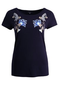 Haut bleu marine à manches courtes avec col rond, présentant des motifs floraux et feuillus brodés symétriques en bleu, blanc, beige et gris à motifs.
