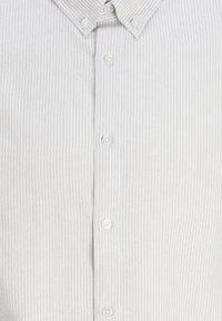Camisa de botones con rayas verticales en blanco y gris claro, cuello extendido y botones frontales, con una textura de algodón suave.