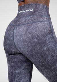 Donkergrijze leggings met een textuurpatroon, hoge tailleband en een klein logo op de achterkant. Naaddetails verbeteren de vorm en pasvorm.