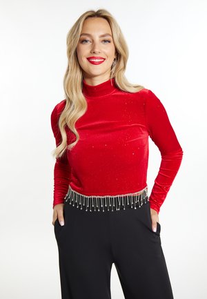 Top a maniche lunghe in velluto rosso con paillettes, caratterizzato da un design aderente e una frangia di perline all'orlo, abbinato a pantaloni neri a vita alta.