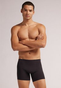 Černé boxerky vyrobené z elastické tkaniny, navržené s bezešvou gumou v pase a přiléhavým střihem, pokrývající horní stehna.