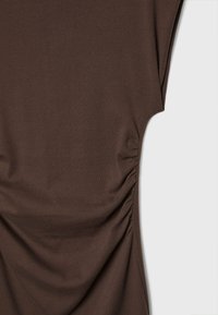 Haut marron ajusté en tissu doux avec un détail froncé sur les côtés, manches courtes et texture lisse.