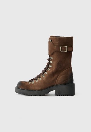 Barna velúr csizma kerek orral, fűzős elülső résszel, fém cipőlyukakkal, bokapánttal csattal, és texturált gumitalppal.