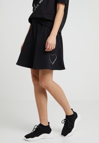 Svart bomullsskjorta med en utsvängd design och sidoficka, prydd med en vit hjärn- grafik med texten "LOVE". Matchad med svarta sportskor.