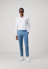 Weißes Hemd mit Knöpfen, hellblaue, maßgeschneiderte Hose, weiße Sneakers und Sonnenbrille. Glattes Material, gerade Passform mit modernem, minimalistischem Design.