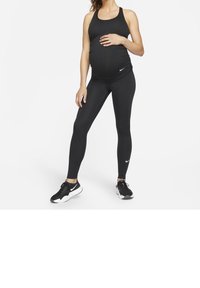 Canottiera nera sportiva e leggings, tessuto elastico, design aderente, con un piccolo logo Nike bianco su entrambi. Sneakers nere e bianche.