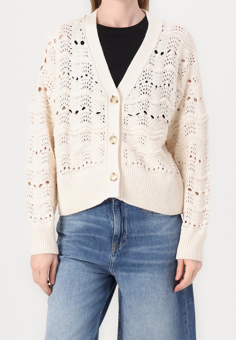 Stickad cardigan i off-white med en vågmönster, V-ringning, knäppning framtill och ribbade ärmslut samt fåll. Passar bra med denim.