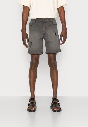 Shorts din denim gri, uzate, cu o croială lejeră, având margini desfăcute, buzunare și cusături vizibile. Potrivite cu sandale negre.