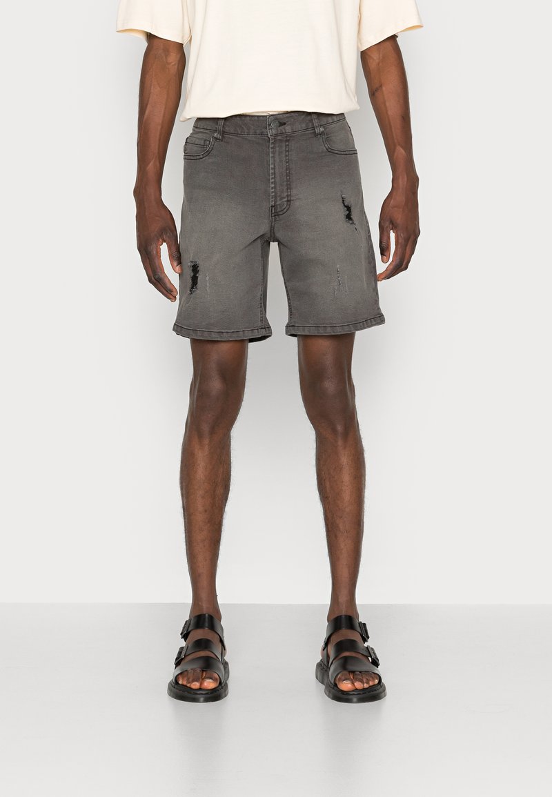 Shorts in denim grigio rovinato con vestibilità morbida, caratterizzati da orli sfrangiati, tasche e cuciture a vista. Abbinati a sandali neri.