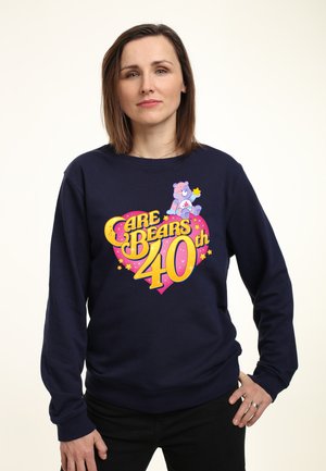 Marineblå sweatshirt med et farverigt "Care Bears 40th" grafik med stjerner og en bjørn illustration, lavet af blødt stof med en afslappet pasform.