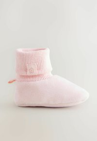 Chausson en tissu rose avec un poignet côtelé, un bout arrondi et une petite languette à l'arrière. Texture douce avec un logo brodé simple sur le poignet.