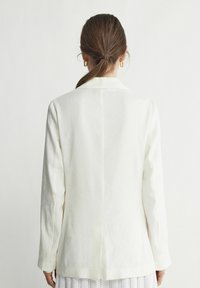 Biały żakiet z klasycznym kołnierzykiem, prostym krojem i długimi rękawami. Wykonany z gładkiego, teksturowanego materiału z subtelnymi detalami szycia.