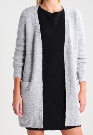 Grijze cardigan met open voorkant, textuur gebreide stof en lange mouwen, gedragen over een zwarte jurk. Bevat twee voorzakken.