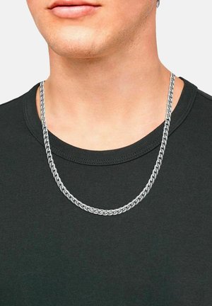 Collana in argento con maglie intrecciate, indossata sopra una maglietta scura. Le maglie sono spesse e presentano una superficie liscia e riflettente.