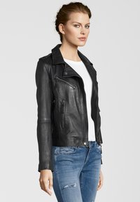 Schwarze Lederbikerjacke mit Reverskragen, Reißverschlusstaschen und taillierter Passform, getragen über einem weißen Hemd und blauen Jeans.