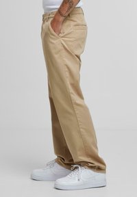 Kaki chinos med løs passform, sidelommer og en baklomme, kombinert med hvite sneakers. Glatt bomullsstoff, rene sting.