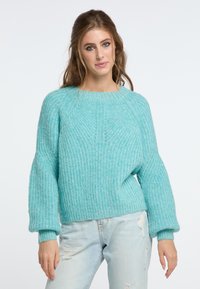 Pulover tricotat teal, cu un design texturat și dantelat. Are un guler rotund și mâneci tip balon. Este asortat cu blugi deschiși, puțin deteriorați.