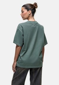 T-shirt verde oversize con scollatura rotonda e maniche corte. Presenta un piccolo dettaglio del logo sul retro. Realizzato in cotone con una texture morbida.