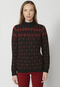 Pull en tricot noir avec un motif géométrique rouge ; col montant, manches longues, texture douce, ourlet et poignets côtelés.