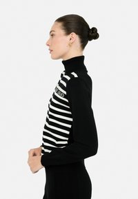 Maglione a collo alto a righe bianche e nere con un design aderente, polsini a coste e un dettaglio decorativo del logo sul petto.