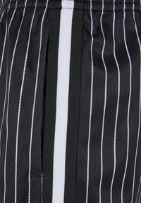 Shorts de sport noirs avec des rayures blanches, dotés d'une texture en maille respirante et d'une ceinture élastique. Comprend une rayure latérale contrastante.