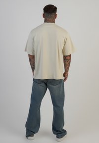 Beeži ülerõhuga t-särk lühikeste varrukatega, sujuva tekstuuriga. Kombineeritud mugava lõikega siniste teksadega. Minimalistlik disain ja casual välimus.