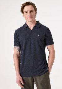 Marineblauwe poloshirt met korte mouwen en een V-hals ontwerp. De stof heeft een zachte textuur. Klein logo op de linkerkant van de borst.