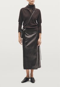 Maglione corto a maniche corte marrone con colletto, abbinato a una gonna midi in pelle nera e scarpe slip-on nere. Inclusa una piccola borsa a tracolla.