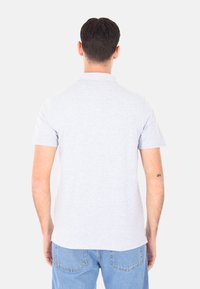 Polo shirt grigio chiaro a maniche corte con una texture morbida, colletto classico e orlo dritto. Indossato con jeans di denim.