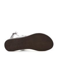 Calzado con una suela de goma texturizada en color marrón, correas grises y una hebilla plateada. El diseño es plano, presentando una silueta simple y elegante.