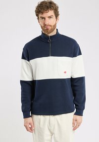 Pull-over zippé bleu marine et blanc, fabriqué en coton, doté d'une poche avant et d'une finition texturée pour un confort et des détails supplémentaires.