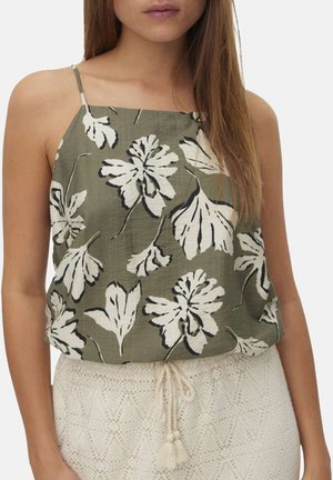 Femme portant un haut sans manches vert olive à imprimé floral blanc et une jupe blanche texturée avec une taille à cordon.