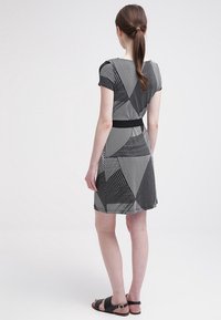 Kortärmad svart och vit klänning med geometriska mönster, med smal midja och avslappnad kjol. Bärs med platta svarta sandaler.