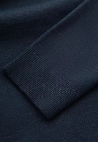 Marineblau gestrickter Stoff mit einem gerippten Bündchen und einer glatten Textur, die feine Details im Webmuster des Textils hervorhebt.