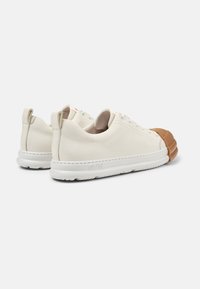 White leather sneakers with a brown rubber toe cap, textured sole, and contrasting loop tab. Features subtle branding and classic lace closure.