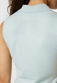 Ljusblå  ärmlös polo med en strukturerad stickning, med perforerade detaljer på baksidan för andningsförmåga och en subtil design.