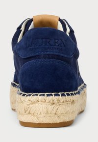 Námořnické semišové tenisky s béžovou espadrillovou podrážkou, koženým akcentem na patě a embosovaným logem. Měkká textura a kulatý tvar pro pohodlí.