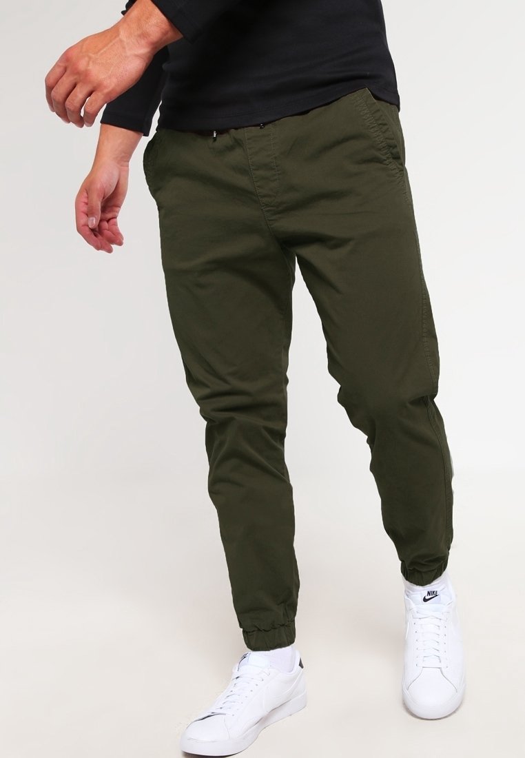 Olijfgroene joggerbroek van lichtgewicht stof met elastische boorden, zijzakken en een taille met trekkoord, gecombineerd met witte sneakers.