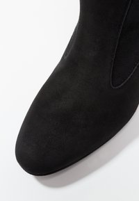 Černá semišová kotníková bota s špičatou špičkou, elastickými bočními panely a hladkou texturou. Podešev je plochá a mírn�ě zakřivená.
