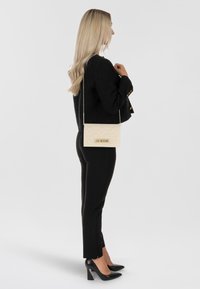 Crossbody bag in cream with a diamond quilted texture; features a chain strap and gold "LOVE MOSCHINO" logo. Worn with black attire and heels.