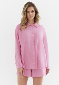 Różowy zestaw odzieży domowej w paski, składający się z koszuli z długim rękawem z kołnierzykiem i pasujących szortów, wykonany z miękkiego materiału.