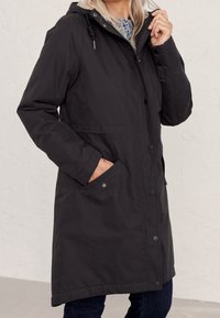 Czarny, długi płaszcz z kapturem, z zapięciem na zamek i guziki, kieszeniami po bokach oraz gładką fakturą. Odpowiedni na różne warunki pogodowe.