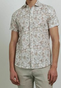 Camisa de botones de manga corta en una tela ligera, con un patrón circular en tonos suaves de beige y gris con una sutil textura.